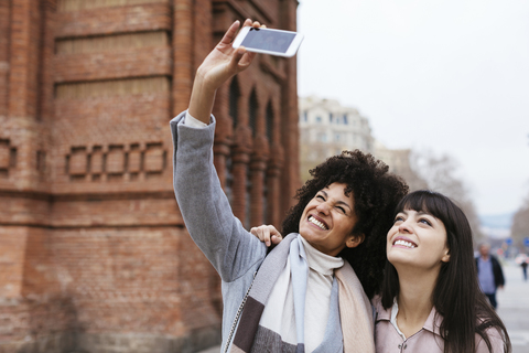 Spain, Barcelona, two happy women taking a selfie at a gate stock photo