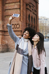 Spain, Barcelona, two playful women taking a selfie at a gate - EBSF02148