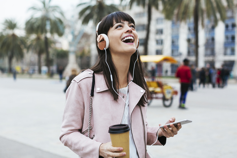 Spain, Barcelona, laughing woman with coffee, cell phone and headphones in the city stock photo