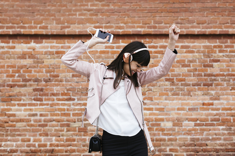 Glückliche Frau mit Handy, die über Kopfhörer an einer Mauer Musik hört, lizenzfreies Stockfoto