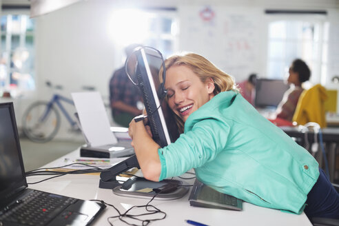 Geschäftsfrau umarmt Computer am Schreibtisch - CAIF01839