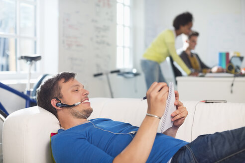 Mann mit Headset macht sich auf dem Sofa Notizen - CAIF01841