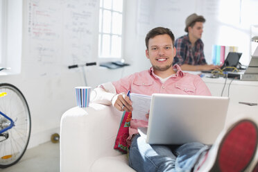 Businessman using laptop on sofa in office - CAIF01855