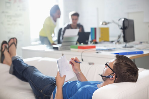 Geschäftsmann macht sich Notizen auf dem Sofa im Büro - CAIF01857