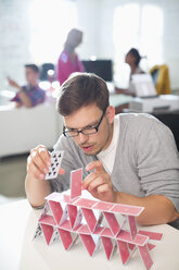 Businessman making house of cards in office - CAIF01870