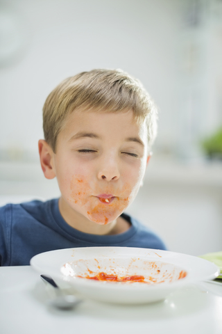Junge schlürft Spaghetti am Tisch, lizenzfreies Stockfoto
