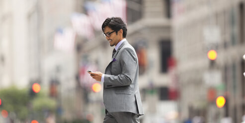 Businessman using cell phone on city street - CAIF02051