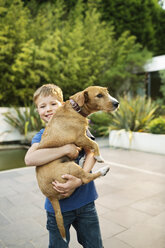Smiling boy holding dog outdoors - CAIF02192