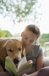 Girl reading with dog in armchair - CAIF02225