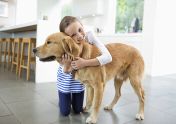 Smiling girl hugging dog in kitchen - CAIF02228