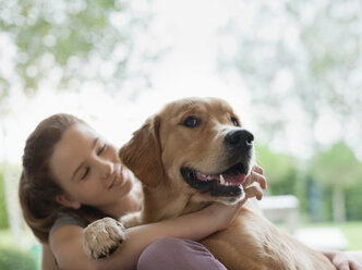 Lächelndes Mädchen umarmt Hund im Freien - CAIF02235