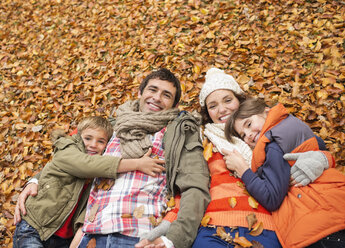 Lächelnde Familie, die im Herbstlaub liegt - CAIF02275