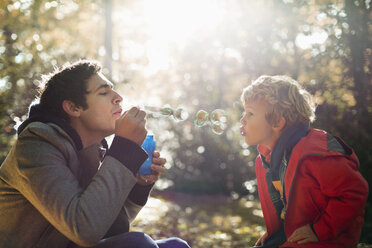 Vater und Sohn beim Blasen von Seifenblasen im Park - CAIF02280