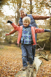 Mann und Enkel spielen auf einem Baumstamm im Park - CAIF02292