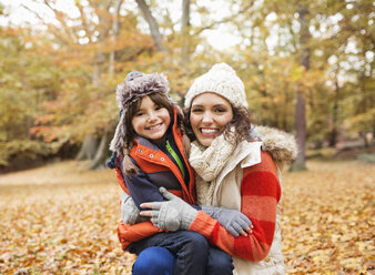 Mother and daughter smiling in autumn leaves - CAIF02300