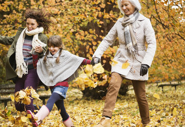 Three generations of women playing in autumn leaves - CAIF02319