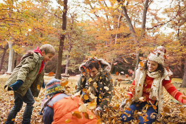 Family playing in autumn leaves in park - CAIF02329