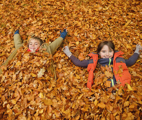 Children laying in autumn leaves - CAIF02340