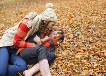 Mother and daughter playing in autumn leaves - CAIF02346