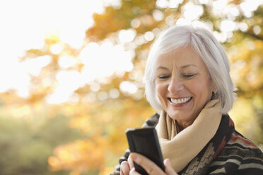 Ältere Frau benutzt Mobiltelefon im Park - CAIF02347