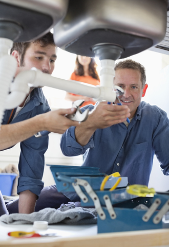 Klempner arbeiten an Rohren unter der Küchenspüle, lizenzfreies Stockfoto