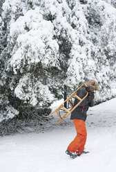 Junge trägt Holzschlitten im Schnee - CAIF02442