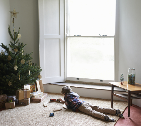 Junge spielt mit Zug am Weihnachtsbaum, lizenzfreies Stockfoto