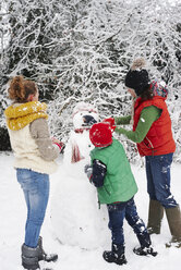 Mutter und Kinder bauen Schneemann im Freien - CAIF02449