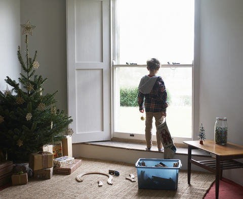 Junge hält Weihnachtsstrumpf am Fenster, lizenzfreies Stockfoto