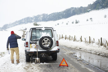 Man working on broken down car in snow - CAIF02456