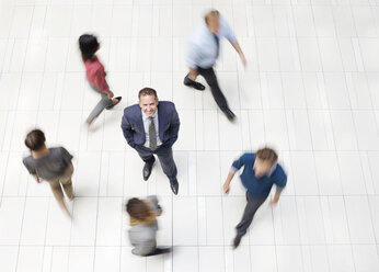 Businessman standing in busy office hallway - CAIF02573