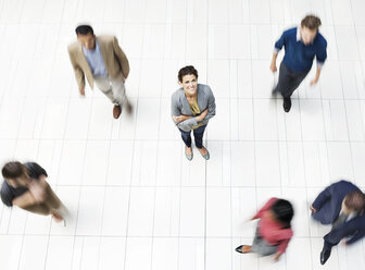 Businesswoman standing in busy office hallway - CAIF02575