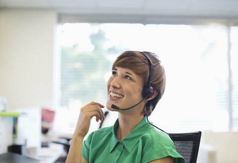 Geschäftsfrau spricht mit Headset am Schreibtisch, lizenzfreies Stockfoto