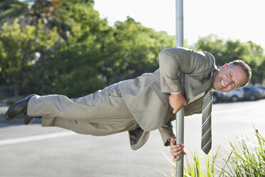 Businessman balancing on pole on city street - CAIF02601