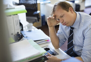 Businessman sighing at desk - CAIF02659