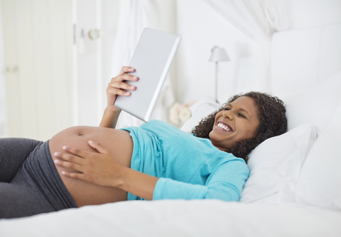 Schwangere Frau mit Tablet-Computer im Bett, lizenzfreies Stockfoto