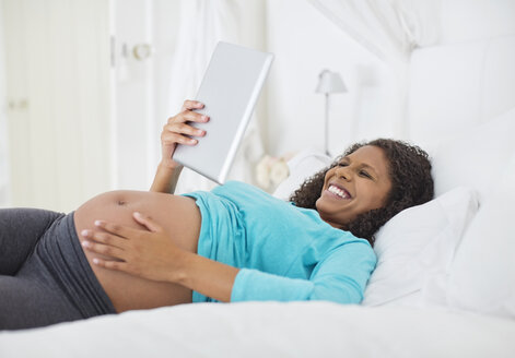 Schwangere Frau mit Tablet-Computer im Bett - CAIF02678