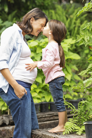 Mädchen küsst schwangere Mutter im Freien, lizenzfreies Stockfoto