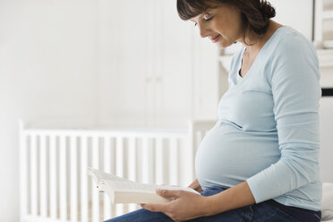 Schwangere Frau liest im Kinderzimmer - CAIF02699