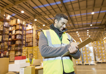 Worker writing on clipboard in warehouse - CAIF02845