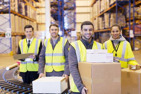 Lächelnde Arbeiter am Förderband im Lager, lizenzfreies Stockfoto