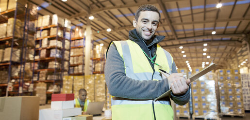 Worker writing on clipboard in warehouse - CAIF02878