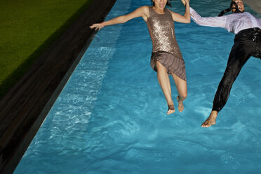 Fully dressed couple jumping into swimming pool - CAIF02886