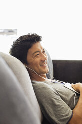 Man listening to headphones on sofa - CAIF02933
