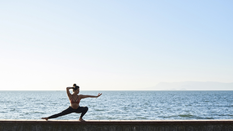 Young woman practicing yoga on a wall by the sea stock photo