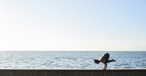 Young woman practicing yoga on a wall by the sea - IGGF00440