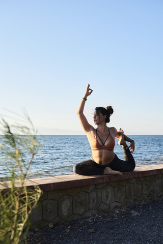 Young woman practicing yoga on a wall by the sea stock photo