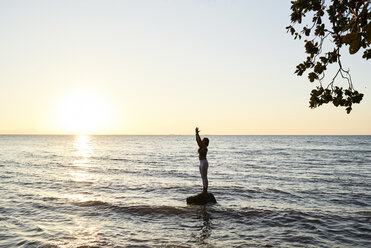 Junge Frau übt Yoga auf einem Felsen im Meer bei Sonnenuntergang - IGGF00446