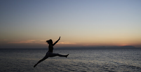 Young woman jumping at the sea at sunset - IGGF00448