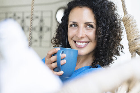 Lächelnde Frau mit lockigem Haar hält eine Tasse Kaffee - SBOF01434
